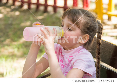 A girl on a bench on a hot day drinking water from a bottle 43726954