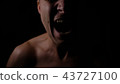 Angry man. A screaming evil expression. Close-up of the man's face in the dark. 43727100