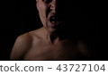 Angry man. A screaming evil expression. Close-up of the man's face in the dark. 43727104