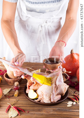 The hands of the cook woman grease the raw chicken sauce on a brown wooden table 43737647