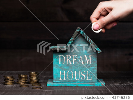 Wooden house model with coins next to it and hand 43746286