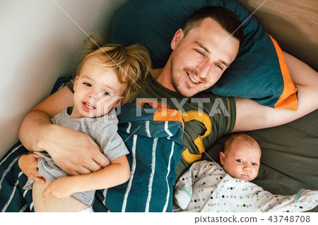 Young man lying in bed with kids Young man lying in bed with kids 43748708