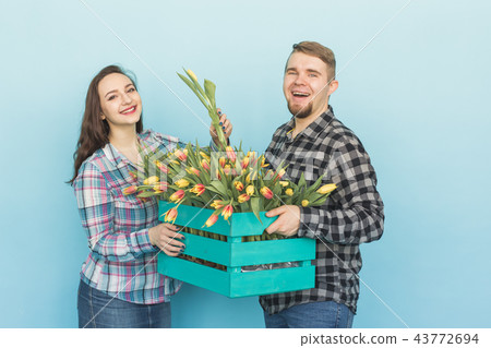 Happy man and woman florists holding box with tulips and laughing on blue background Happy man and woman florists holding box with tulips and laughing on blue background 43772694