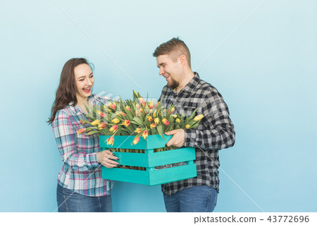 Happy man and woman florists holding box with tulips and laughing on blue background 43772696