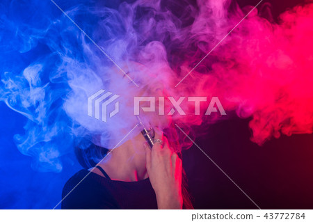 Portrait of young woman in neon blue and red smoke with vape or e-cigarettes 43772784