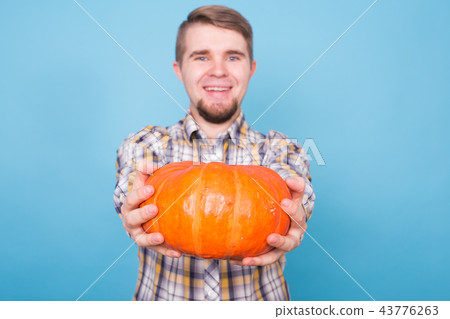 Autumn, harvest and agriculture concept - Smiling man holding pumpkins over blue background. Autumn, harvest and agriculture concept - Smiling man holding pumpkins over blue background. 43776263