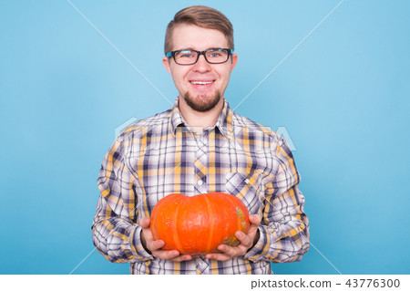 People, holidays and autumn concept - handsome man holding pumpkins on blue background People, holidays and autumn concept - handsome man holding pumpkins on blue background 43776300