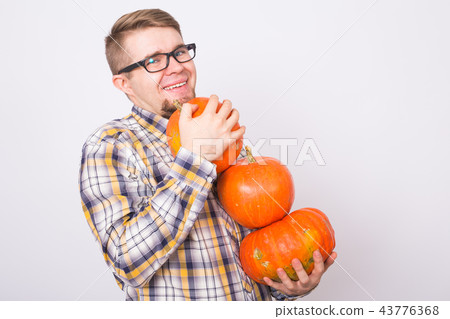 Farm, autumn, people concept - young happy man farmer in glasses with pumpkins smiling over the Farm, autumn, people concept - young happy man farmer in glasses with pumpkins smiling over the 43776368