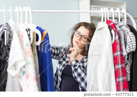 Beauty, fashion and people concept - Beautiful serious woman in black glasses chooses dresses 43777321