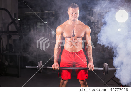 Muscular young man lifting weights in gym Muscular young man lifting weights in gym 43777628