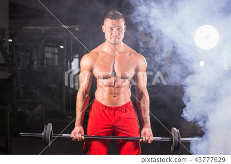 Bodybuilder doing the exercises with barbell. Strong male with naked torso on dark background 43777629
