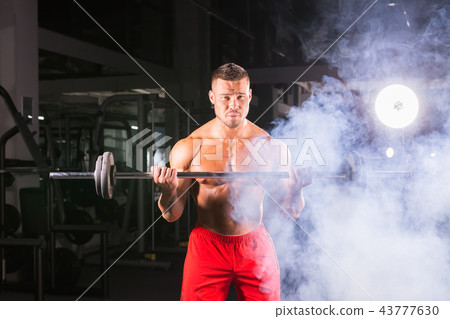 Bodybuilder doing the exercises with barbell. Strong male with naked torso on dark background 43777630