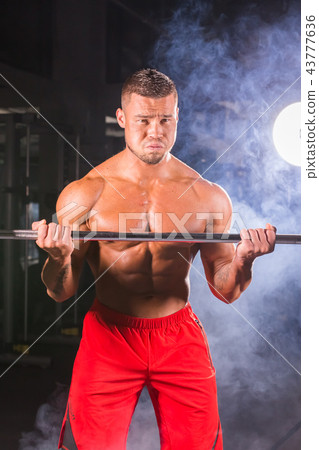 Bodybuilder doing the exercises with barbell. Strong male with naked torso on dark background 43777636