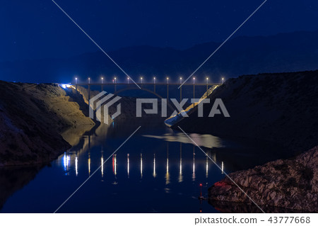 Illuminated highway bridge under stars, reflection of lights in water, mountains in background and Illuminated highway bridge under stars, reflection of lights in water, mountains in background and 43777668