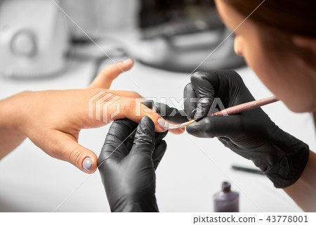 Close-up of master manicurist hands applying light violet varnish on client woman nails using brush. Close-up of master manicurist hands applying light violet varnish on client woman nails using brush. 43778001