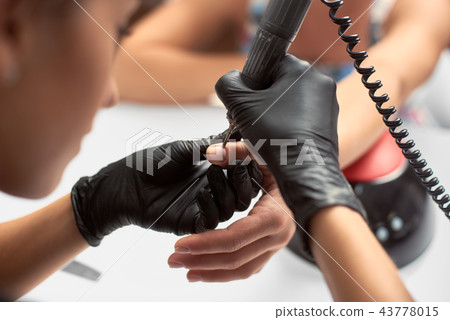 Close-up of professional beautician hands working with electric drill file on client fingernails. Close-up of professional beautician hands working with electric drill file on client fingernails. 43778015