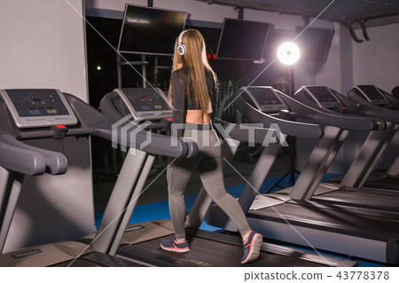 Fitness woman running on treadmill. Girl with muscular legs in gym 43778378
