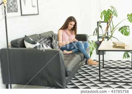 Technologies, people concept - young woman sitting on sofa and watching the tablet or surfing the Technologies, people concept - young woman sitting on sofa and watching the tablet or surfing the 43785756