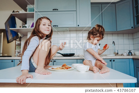 Two little girls in the kitchen sitting on the table. Two little girls in the kitchen sitting on the table. 43786107