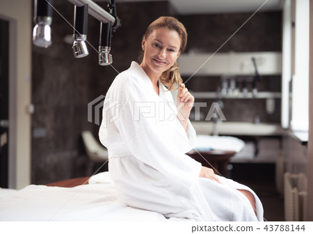 Joyful middle aged woman sitting on daybed at spa salon Joyful middle aged woman sitting on daybed at spa salon 43788144