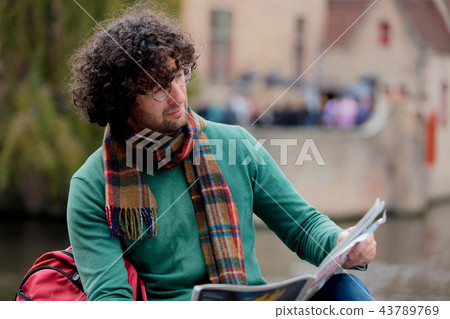 Young man reading a newspaper sitting on bridge Young man reading a newspaper sitting on bridge 43789769