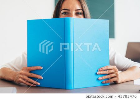 Pretty young woman peeking out of a book and looking at camera Pretty young woman peeking out of a book and looking at camera 43793476