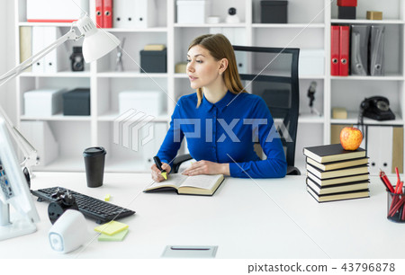 A young girl sits at a computer desk and holds a yellow marker in her hand. Before the girl lies an 43796878