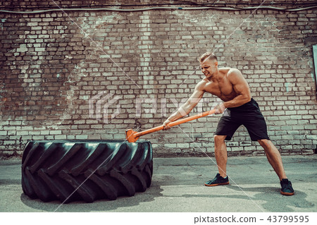 Sport Fitness Man Hitting Wheel Tire With Hammer Sledge Cross fit Training. Sport Fitness Man Hitting Wheel Tire With Hammer Sledge Cross fit Training. 43799595