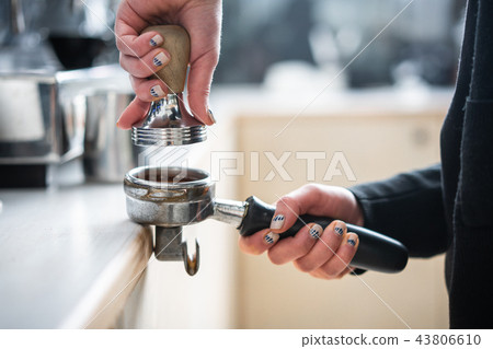 Barista presses ground coffee using tamper. Barista presses ground coffee using tamper. 43806610