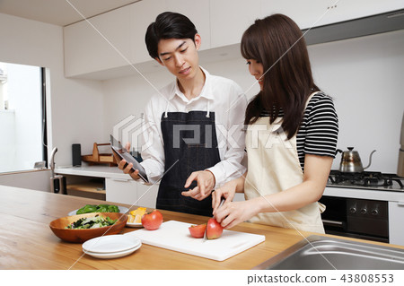 Couple searching the net with a tablet on the tablet and cooking 43808553