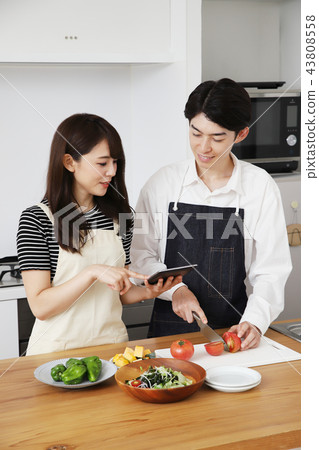 Couple searching the net with a tablet on the tablet and cooking 43808558