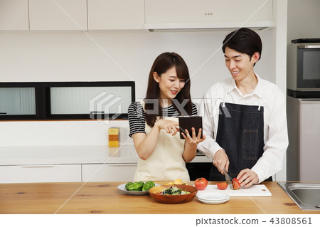 Couple searching the net with a tablet on the tablet and cooking 43808561