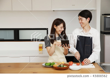 Couple searching the net with a tablet on the tablet and cooking 43808562