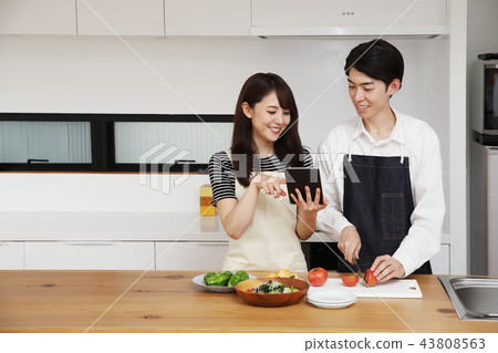 Couple searching the net with a tablet on the tablet and cooking 43808563