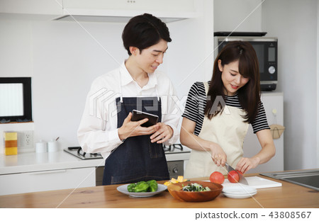 Couple searching the net with a tablet on the tablet and cooking 43808567