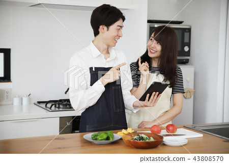 Couple searching the net with a tablet on the tablet and cooking 43808570