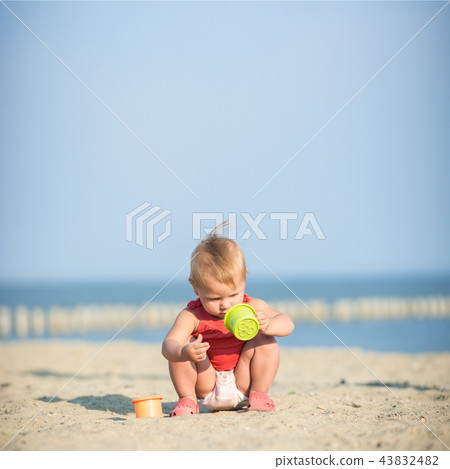 Baby girl in red dress playing on sandy beach near the sea.  43832482