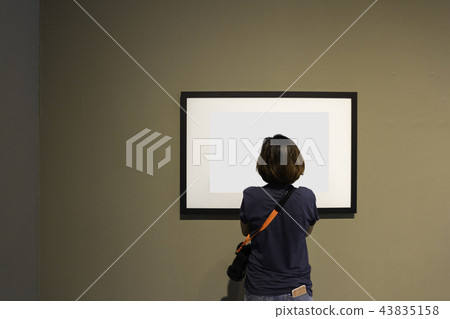 Woman is looking at blank photo frame on wall Woman is looking at blank photo frame on wall 43835158