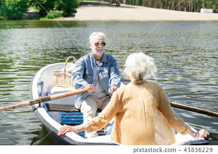 Happy pensioner smiling to his wife while rowing the boat Happy pensioner smiling to his wife while rowing the boat 43836229