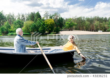 Happy aged woman touching water and her husband rowing the boat Happy aged woman touching water and her husband rowing the boat 43836231