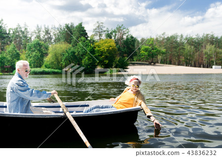 Senior man rowing the boat while his curious wife touching the water 43836232