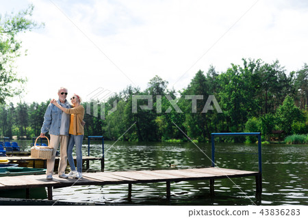 Two senior people hugging on the pier and looking relaxed Two senior people hugging on the pier and looking relaxed 43836283