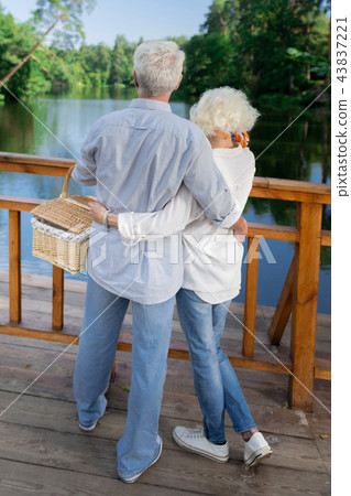 Elderly couple holding picnic basket and looking at the river Elderly couple holding picnic basket and looking at the river 43837221