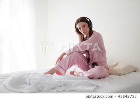 woman in pink Pajamas listening to music with headphones 43842755