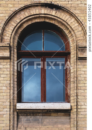 Vintage arched window in the wall of yellow brick. Black glass in a maroon dark red wooden frame 43851402