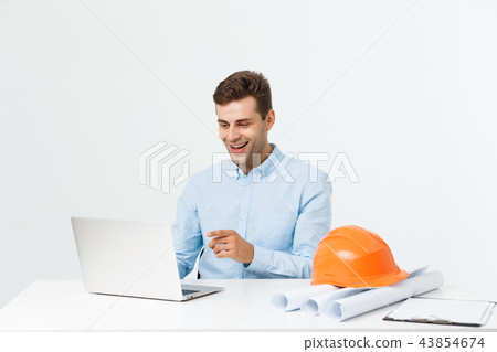 Handsome male engineer is using a notebook for work. He is sitting at the desk and smiling. Copy 43854674