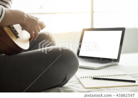 Happy young asian woman playing ukulele sitting on bed in bedroo 43862597