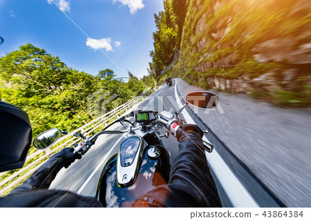 Motorcycle driver riding in Alpine highway, handlebars view, Austria, Europe. Motorcycle driver riding in Alpine highway, handlebars view, Austria, Europe. 43864384