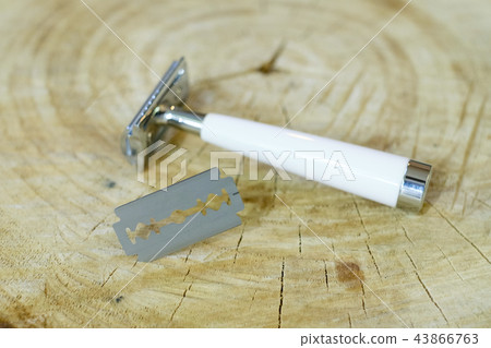 A traditional steel razor with a white bone handle and a steel razor blade on a natural wood 43866763