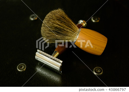 A traditional steel razor with a brown handle of precious wood and a shaving brush on a natural wood A traditional steel razor with a brown handle of precious wood and a shaving brush on a natural wood 43866797